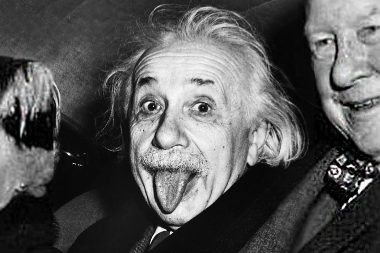 Albert Einstein in the back of a car, hair wild, sticking his tongue out at the camera